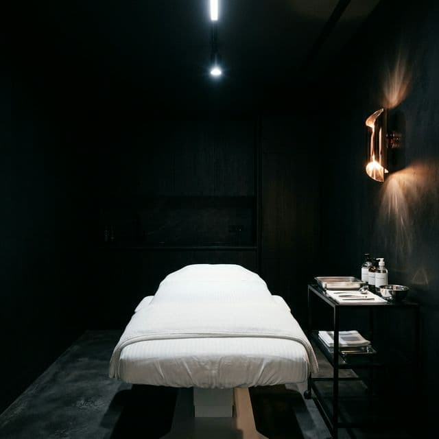 A medical spa treatment room with a white bed under cool LED light and a rose-gold sconce — the context of a med spa installation.